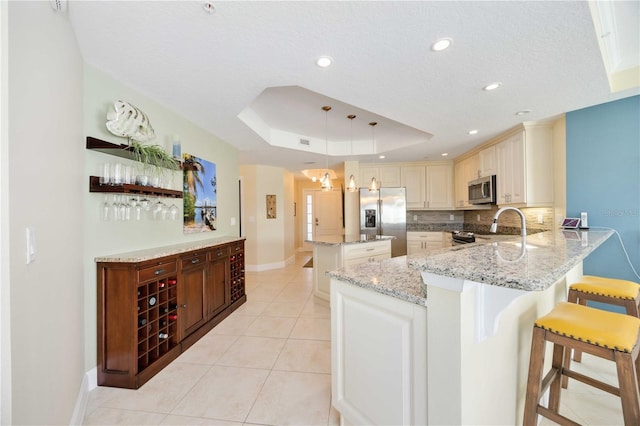 kitchen featuring appliances with stainless steel finishes, a kitchen breakfast bar, a raised ceiling, decorative light fixtures, and kitchen peninsula