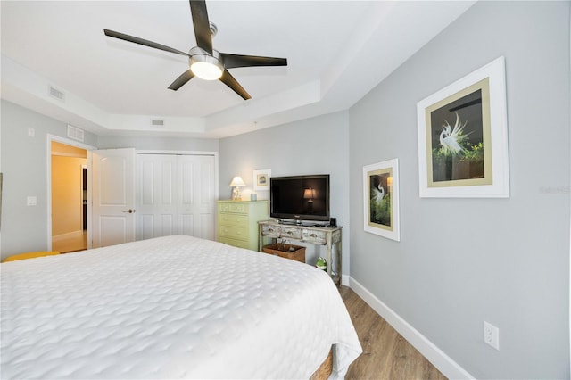 bedroom featuring a tray ceiling, wood-type flooring, a closet, and ceiling fan