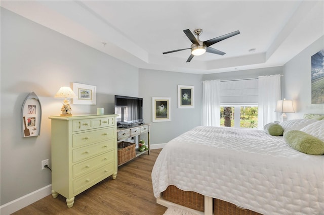 bedroom with ceiling fan, dark hardwood / wood-style floors, and a raised ceiling