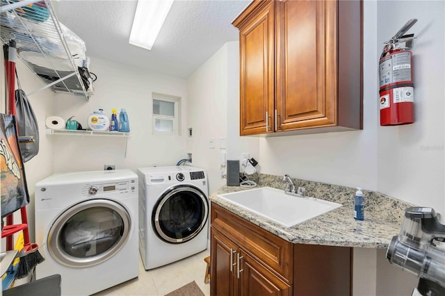 laundry area with light tile patterned flooring, washer and dryer, sink, cabinets, and a textured ceiling