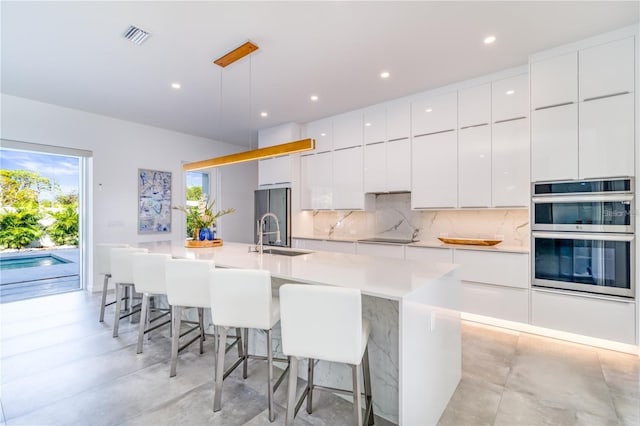 kitchen with white cabinetry, decorative light fixtures, a kitchen bar, and an island with sink