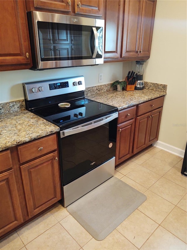 kitchen with light tile patterned flooring, light stone countertops, and stainless steel appliances