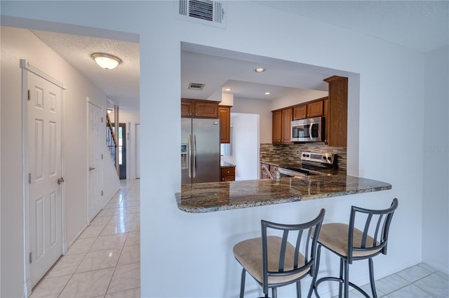 kitchen featuring dark stone counters, a breakfast bar area, kitchen peninsula, and stainless steel appliances