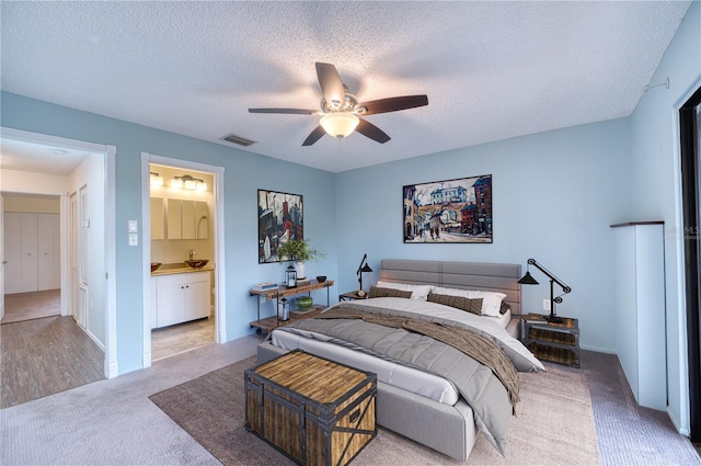 carpeted bedroom with ceiling fan, a textured ceiling, and ensuite bathroom