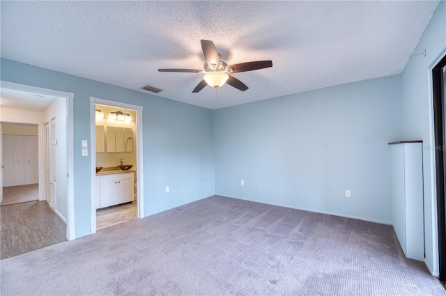 unfurnished bedroom with light carpet, ceiling fan, a textured ceiling, and connected bathroom