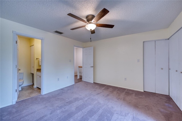 unfurnished bedroom featuring ceiling fan, light colored carpet, ensuite bathroom, and a closet