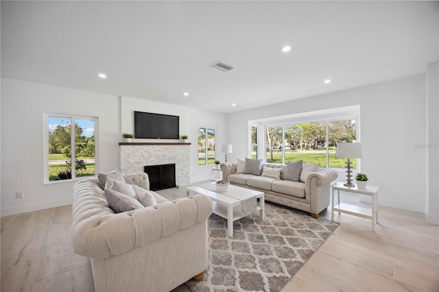 living room featuring a stone fireplace, plenty of natural light, and light hardwood / wood-style flooring