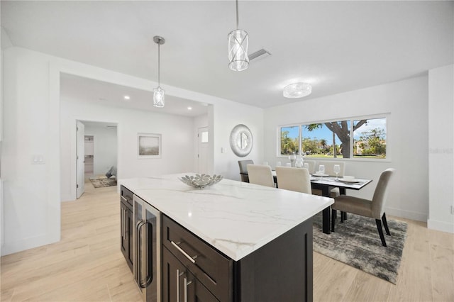 kitchen with hanging light fixtures, wine cooler, light hardwood / wood-style flooring, and light stone counters