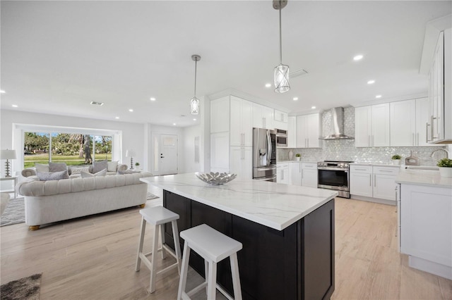 kitchen featuring stainless steel appliances, light hardwood / wood-style floors, white cabinets, wall chimney exhaust hood, and pendant lighting