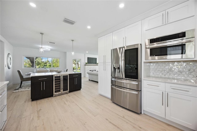 kitchen with appliances with stainless steel finishes, backsplash, hanging light fixtures, beverage cooler, and white cabinets