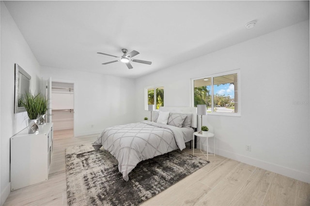 bedroom with ceiling fan, a closet, light wood-type flooring, and a walk in closet