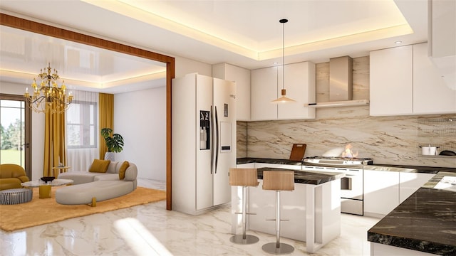 kitchen featuring pendant lighting, wall chimney range hood, a tray ceiling, white cabinetry, and white appliances