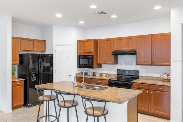 kitchen with black appliances, light tile patterned flooring, a center island with sink, sink, and a breakfast bar