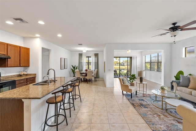 kitchen with a center island with sink, light stone counters, sink, light tile patterned floors, and a kitchen breakfast bar