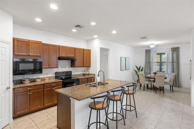 kitchen featuring black appliances, dark stone counters, sink, a breakfast bar area, and a kitchen island with sink