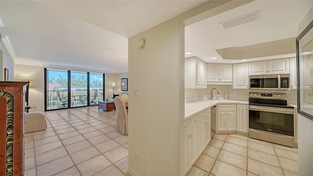 kitchen featuring stainless steel appliances, ornamental molding, sink, light tile patterned floors, and white cabinets