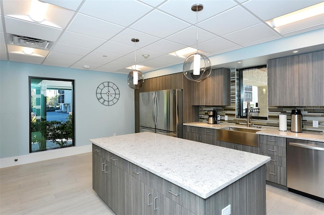 kitchen with a kitchen island, hanging light fixtures, appliances with stainless steel finishes, a paneled ceiling, and tasteful backsplash