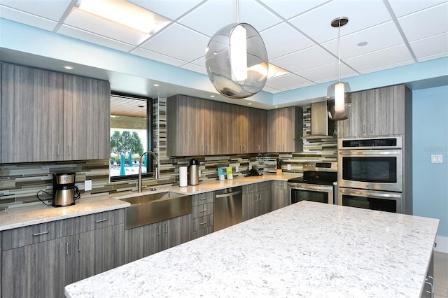 kitchen with wall chimney range hood, decorative light fixtures, tasteful backsplash, and stainless steel appliances