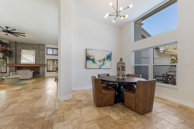 dining room featuring a towering ceiling, ceiling fan with notable chandelier, and a stone fireplace