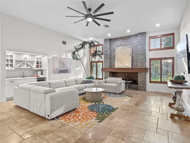 living room featuring a stone fireplace, wet bar, ceiling fan, and a towering ceiling