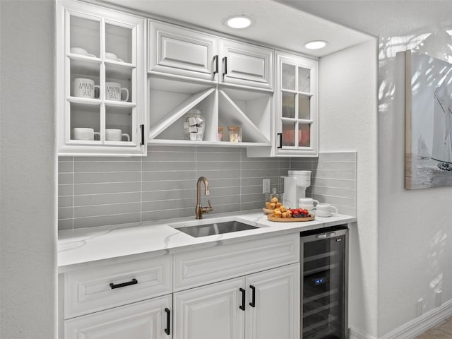 bar with white cabinetry, backsplash, light stone countertops, sink, and beverage cooler