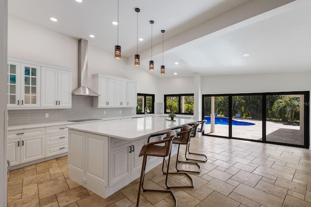 kitchen featuring white cabinetry, a wealth of natural light, wall chimney range hood, and a kitchen island