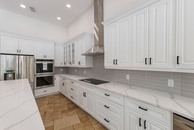 kitchen featuring stainless steel appliances, wall chimney range hood, white cabinetry, and light stone counters