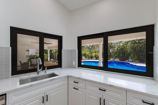 kitchen with tasteful backsplash, light stone countertops, sink, and white cabinets