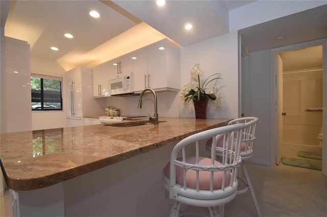 kitchen with white cabinets, kitchen peninsula, sink, a breakfast bar, and dark stone countertops