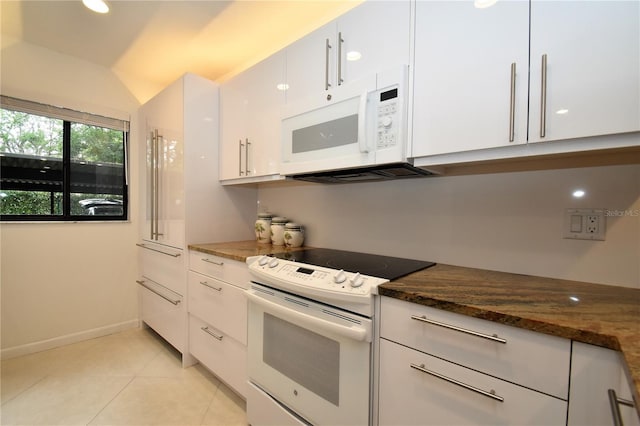 kitchen with dark stone counters, vaulted ceiling, light tile patterned floors, white cabinetry, and white appliances