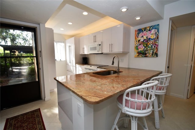 kitchen featuring white cabinetry, sink, a breakfast bar, kitchen peninsula, and white appliances