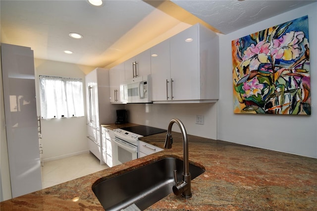 kitchen with dark stone counters, light tile patterned floors, sink, white cabinets, and white appliances