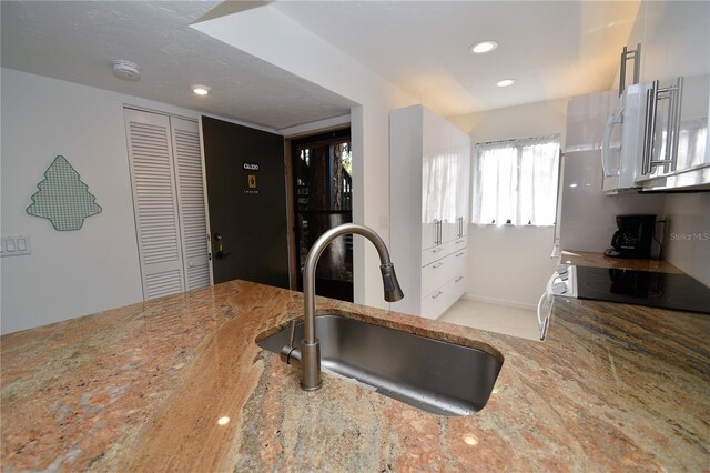 kitchen with black stove, sink, and white cabinets