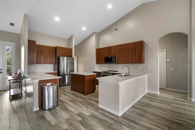 kitchen featuring a kitchen island, hardwood / wood-style flooring, kitchen peninsula, stainless steel appliances, and high vaulted ceiling