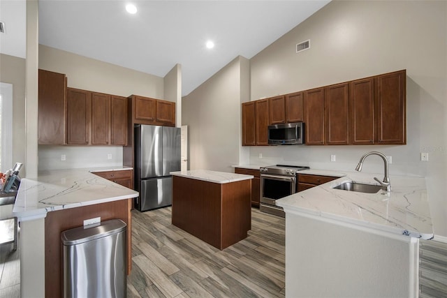 kitchen featuring kitchen peninsula, stainless steel appliances, sink, light hardwood / wood-style floors, and a center island