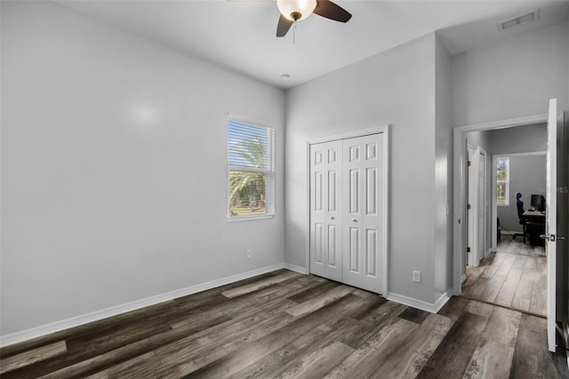 unfurnished bedroom featuring a closet, ceiling fan, multiple windows, and dark hardwood / wood-style floors