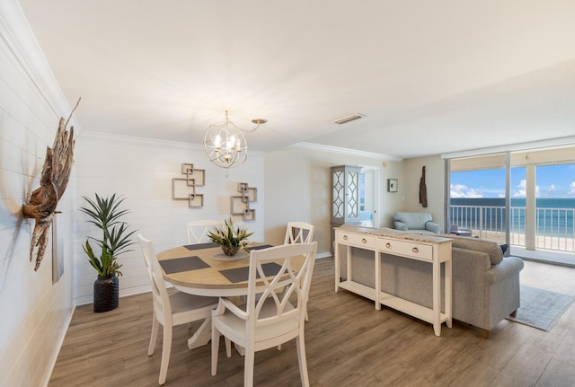 dining room with hardwood / wood-style floors, crown molding, a water view, and a chandelier