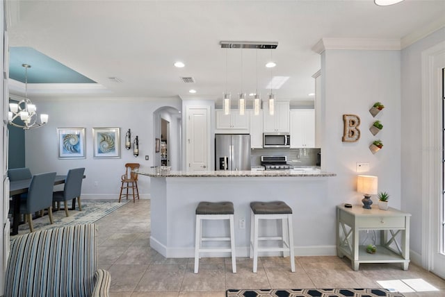 kitchen with kitchen peninsula, light stone countertops, white cabinets, decorative light fixtures, and appliances with stainless steel finishes