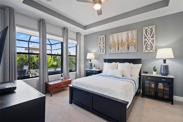 bedroom with a raised ceiling, light carpet, and ceiling fan