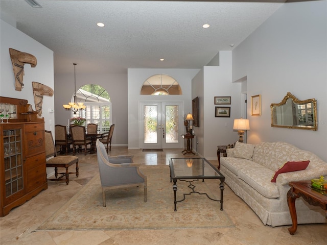 living room with french doors, a high ceiling, a textured ceiling, and a chandelier