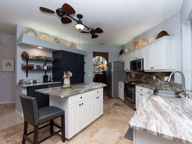 kitchen with stainless steel appliances, white cabinets, sink, a kitchen island, and light stone countertops