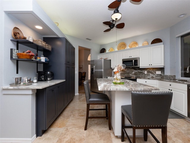 kitchen with stainless steel appliances, white cabinetry, light stone countertops, ceiling fan, and a center island