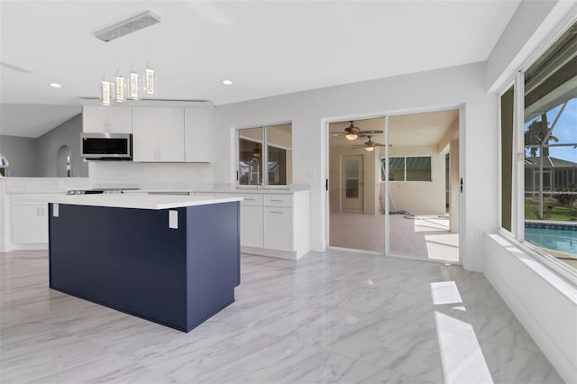 kitchen featuring pendant lighting, ceiling fan with notable chandelier, white cabinets, and a center island