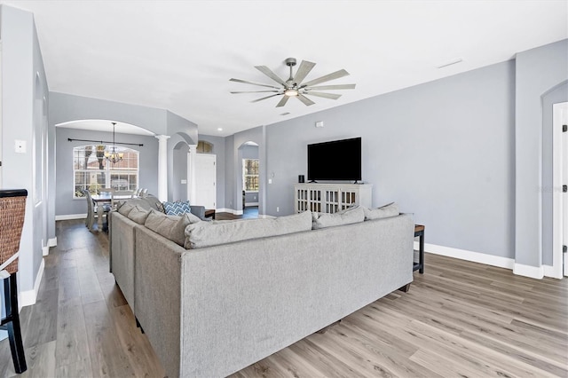 living room featuring ornate columns, ceiling fan with notable chandelier, and light hardwood / wood-style floors