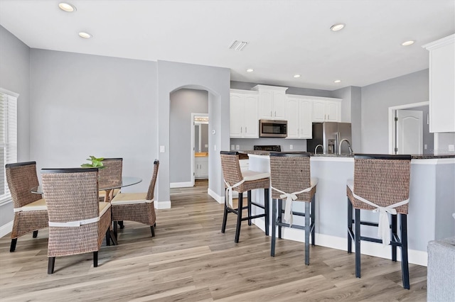 kitchen featuring kitchen peninsula, white cabinetry, a kitchen bar, light hardwood / wood-style flooring, and stainless steel appliances