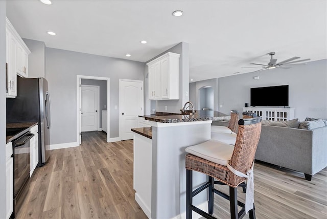 kitchen featuring black stove, kitchen peninsula, ceiling fan, white cabinets, and light hardwood / wood-style flooring