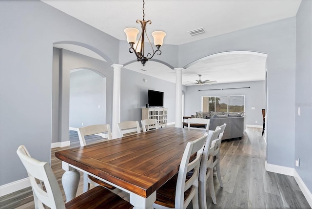 dining room featuring dark hardwood / wood-style floors, ceiling fan with notable chandelier, and decorative columns