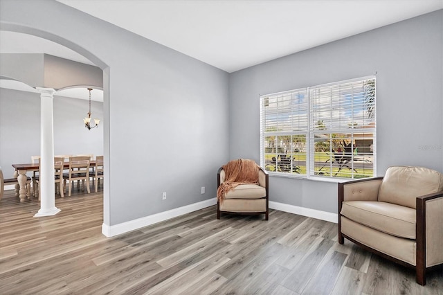 sitting room featuring a notable chandelier, decorative columns, and light wood-type flooring