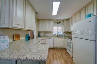 kitchen featuring white appliances, light stone countertops, sink, light wood-type flooring, and kitchen peninsula