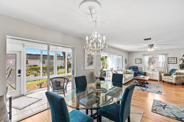 dining space featuring light wood-type flooring, ceiling fan with notable chandelier, and a healthy amount of sunlight